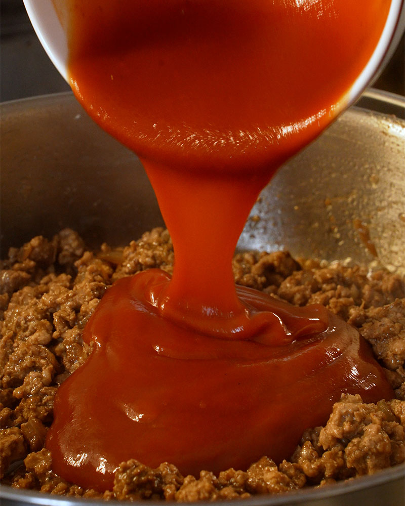 Tomato sauce poured into ground pork mixture for Giniling